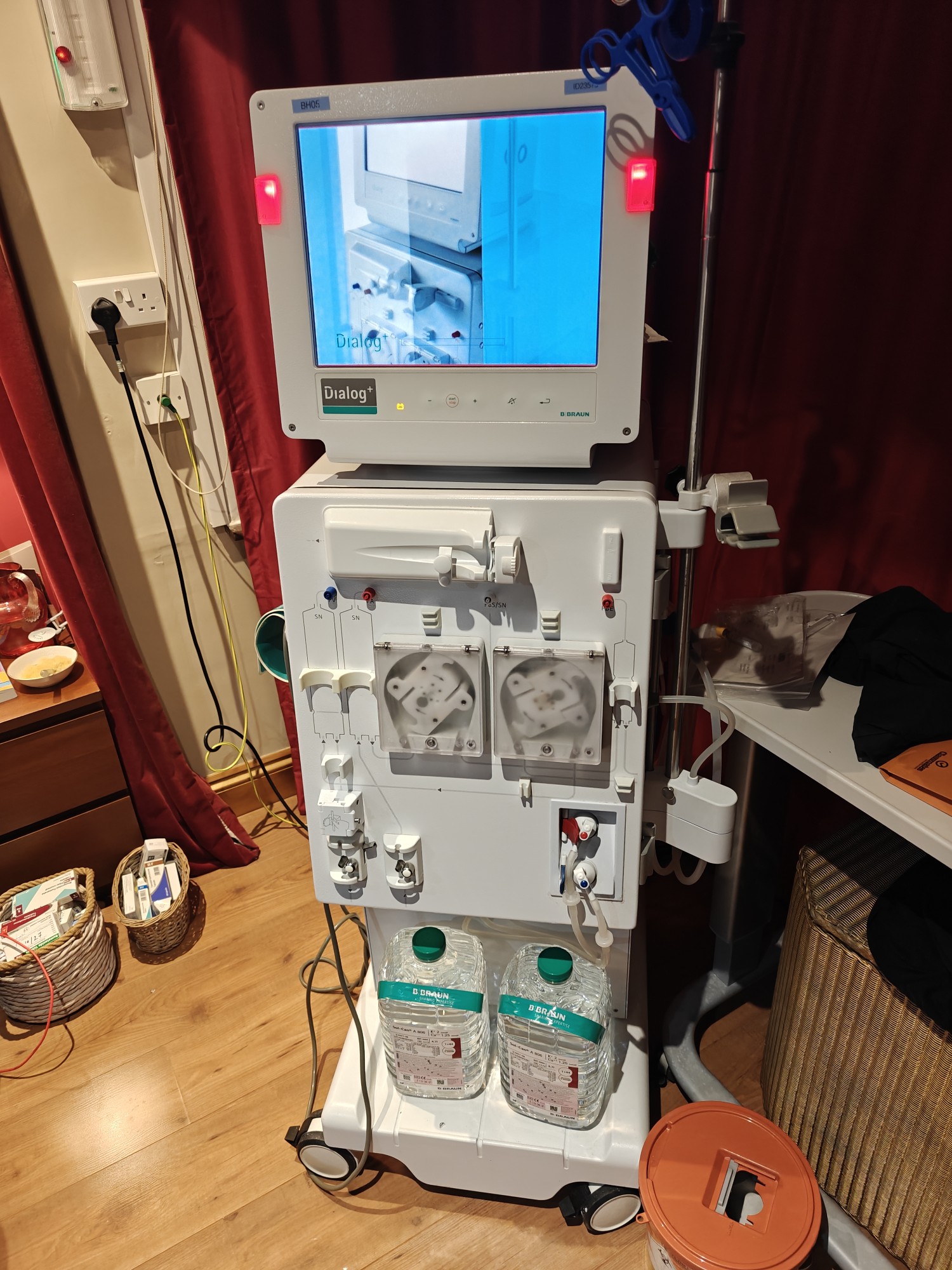 A picture of a dialysis machine starting up. It's about 5ft tall, on wheels, and had two rotary wheels in the middle amid many ports and wires. It has a screen at the top to control the machine. 