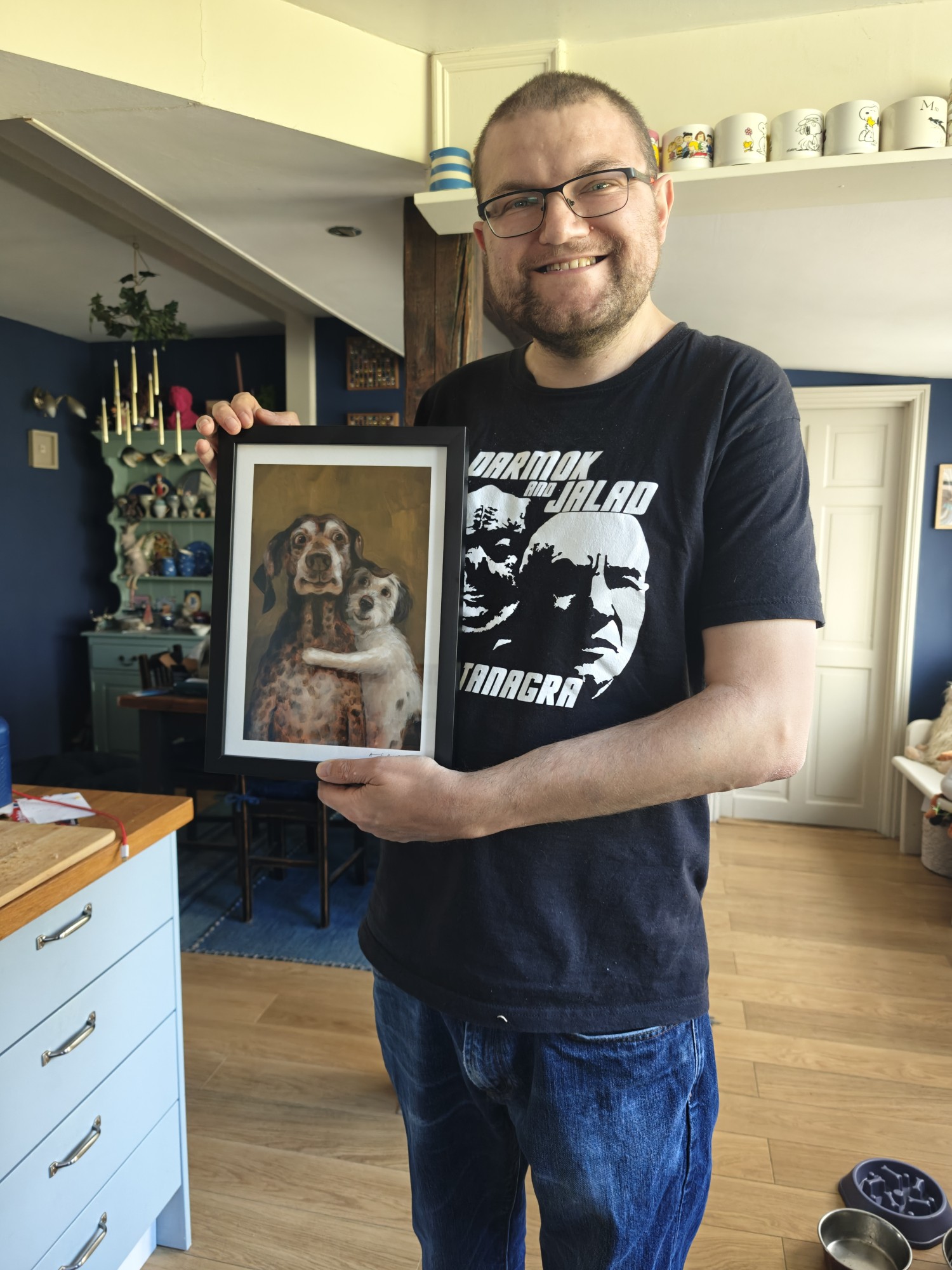 A picture of me holding a print artwork of 2 dogs hugging. I am wearing a black Star Trek t-shirt. 