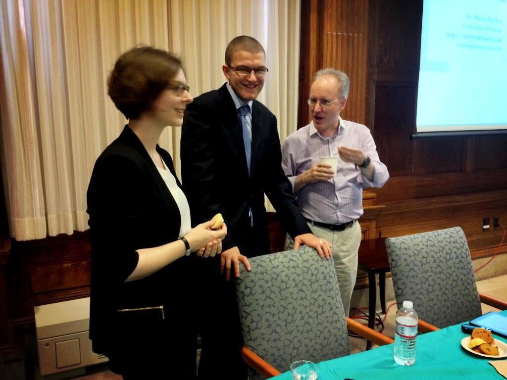 From left to right, a picture of Prof Caroline Edwards, me (Prof Martin Paul Eve) and Prof David Armitage, a Harvard historian. We are all standing and smartly dressed. There is a table in front of us with a bottle of water on it and a plate with some kind of foodstuff. There are two chairs behind the table and I, in the middle, have my hands on the top back of one chair.