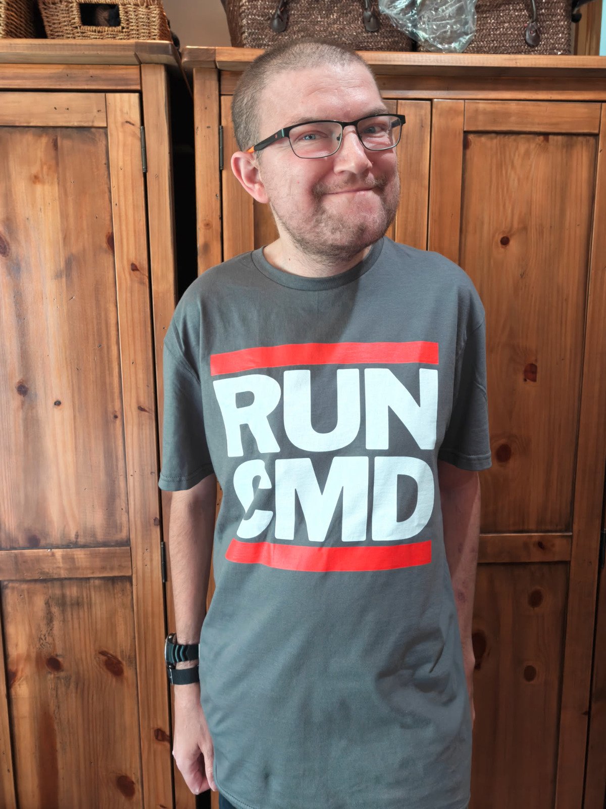 Me, standing in front of a wardrobe, wearing a t-shirt with the logo from RUN DMC, except it says RUN CMD (a geeky computer joke). I am a white male wearing glasses with ultra-short hair. I am very thin. In fact, far too thin and malnourished.