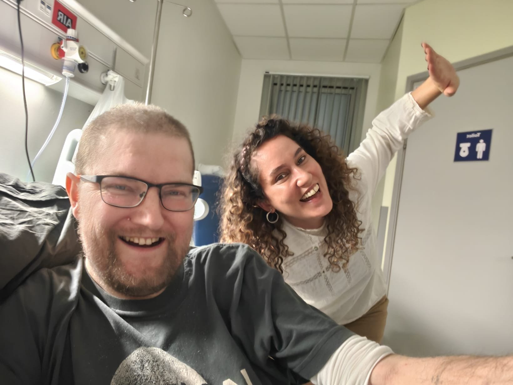 A picture of me, Martin Paul Eve, and Paula Clemente Vega in a hospital room - we are smiling and happy and Paula is tilting her body and raising her arm in an amusing way. We are both laughing.